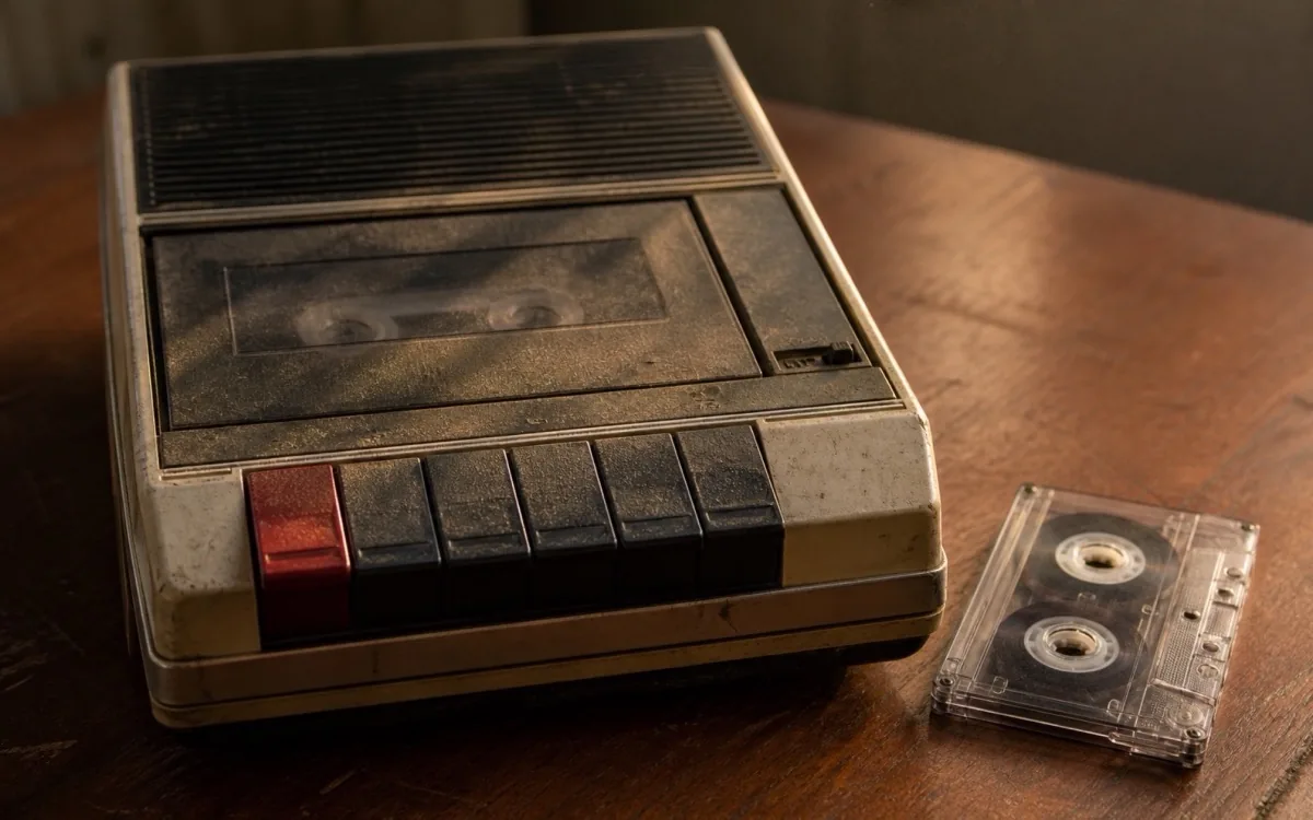 An old cassette recorder on a wooden table, a tape beside it.